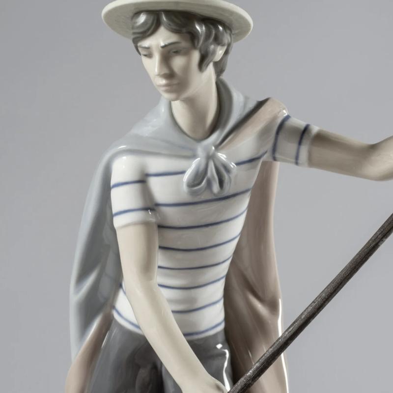 In The Gondola Couple Sculpture. Numbered Edition  Numbered glossy porcelain sculpture of a gondola with young bride and groom enjoying a walk and gondolier in typical striped t-shirt and straw hat attire. 01001350